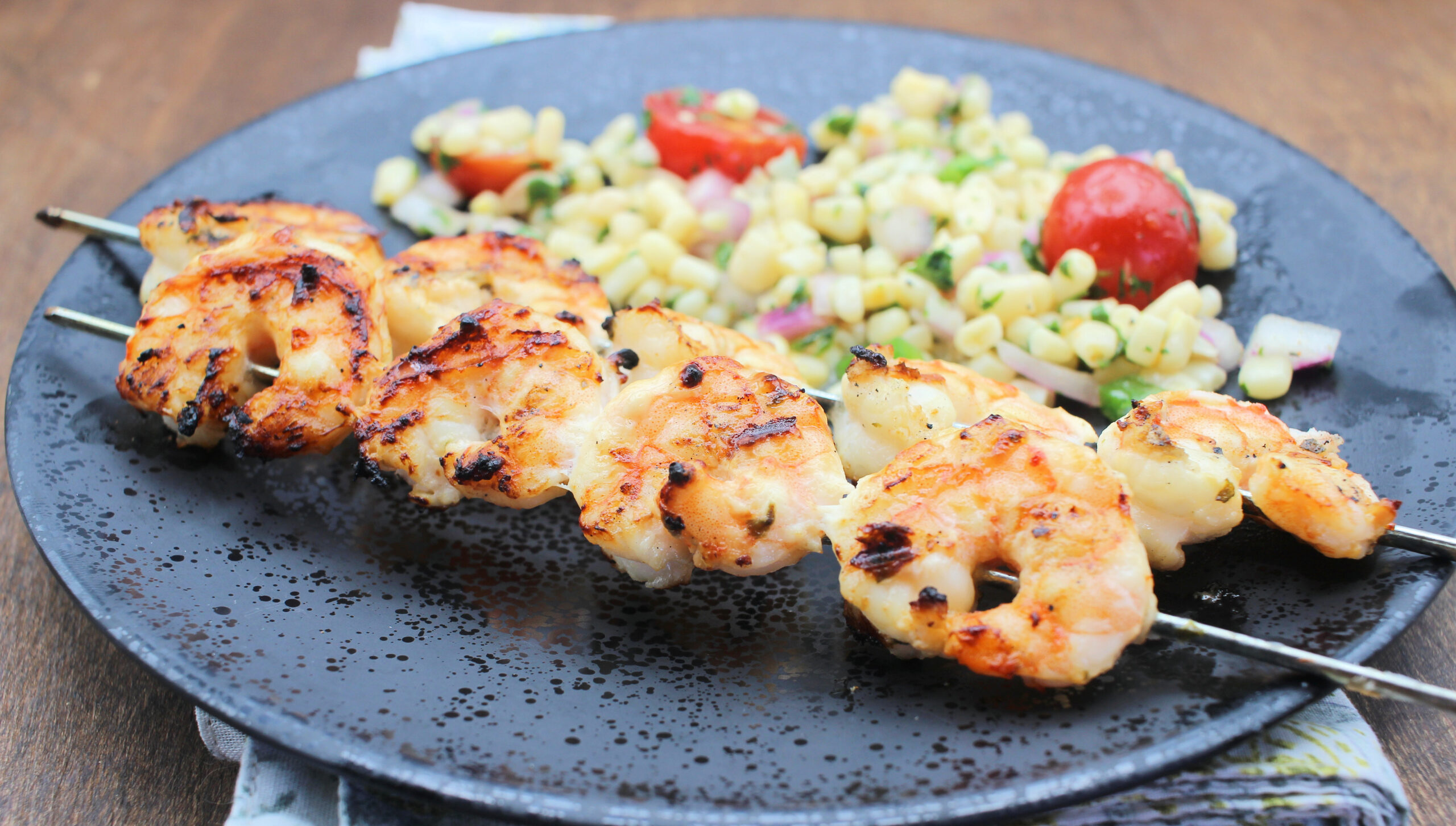 image: shrimp on skewers on a plate with tomatoes and corn.