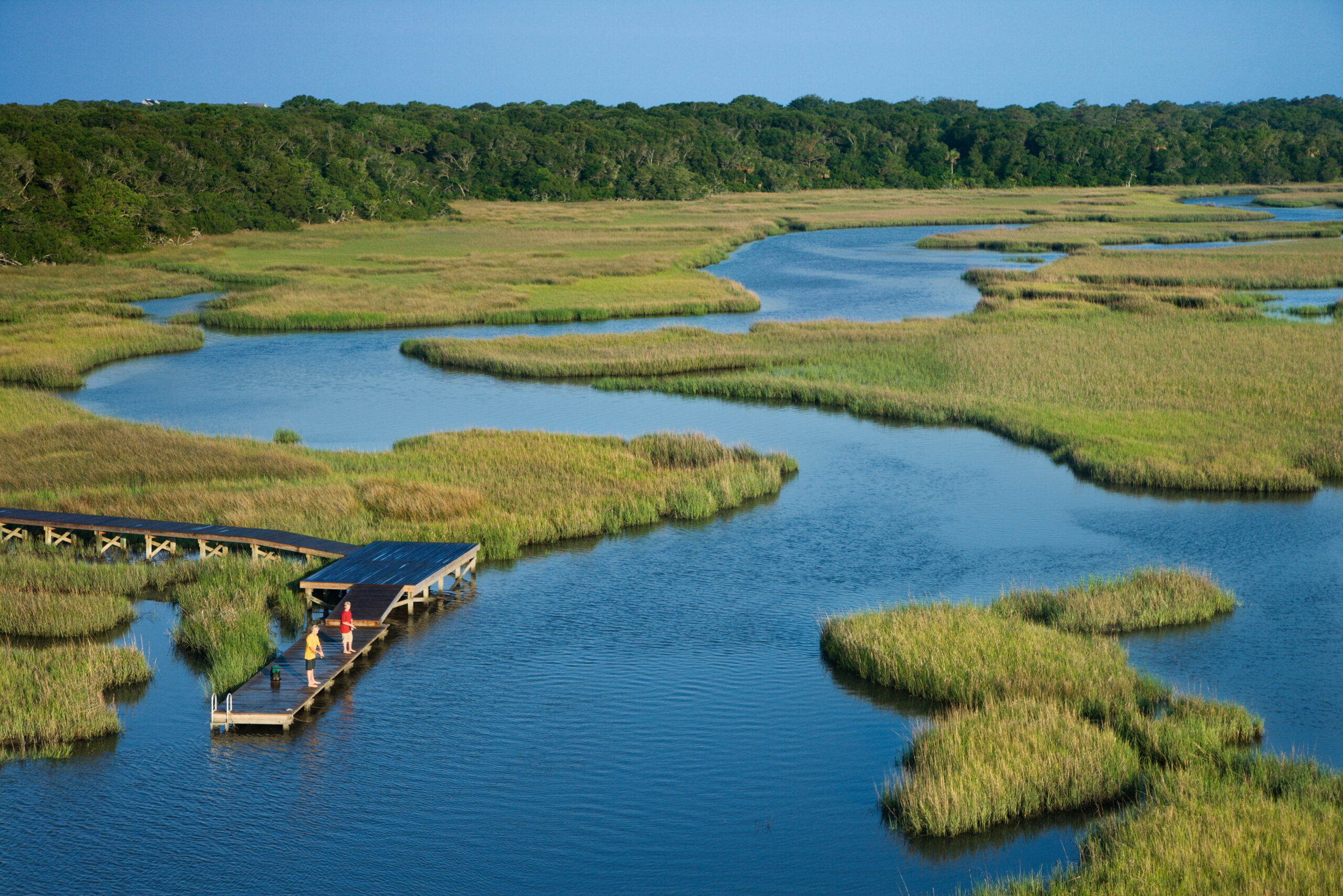 Aerial view of two boys fishing on a dock in a marsh 